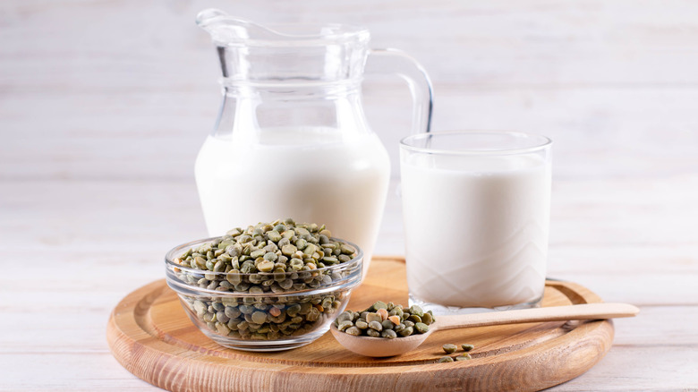 Pea milk in glass pitcher on wooden platter with dried peas in glass bowl