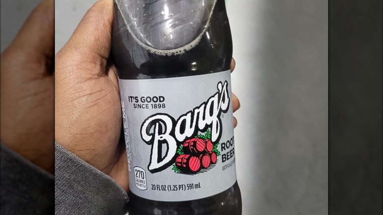 A hand holding a bottle of Barq's root beer
