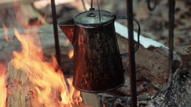 A metal coffee pot hanging over a campfire