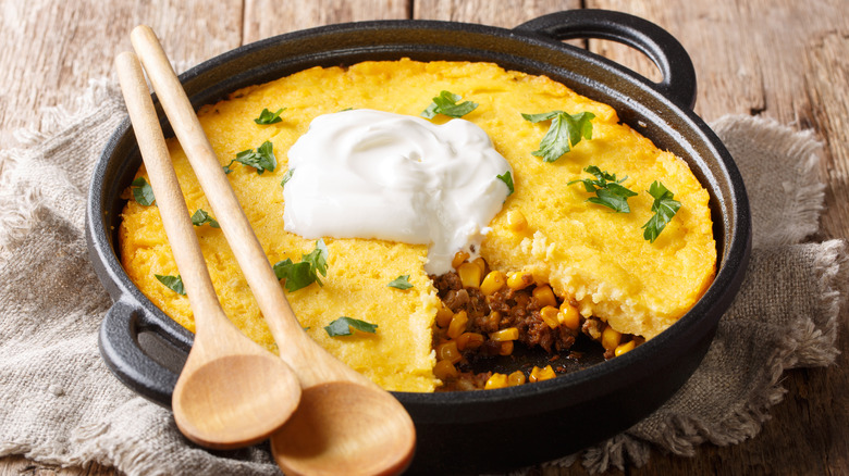 Tamale pie in skillet with wooden spoons