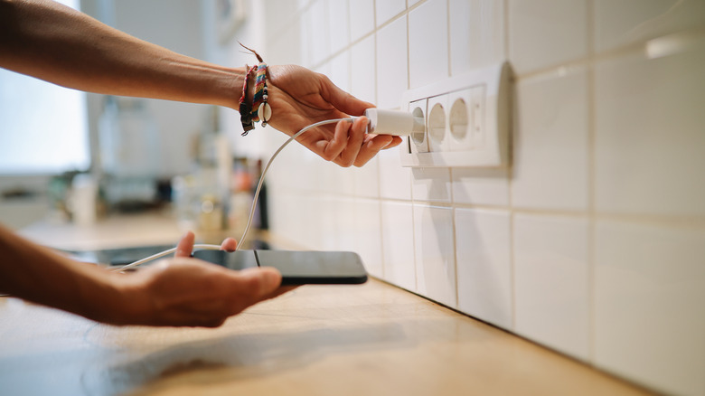 Hands plugging a charger into a kitchen outlet