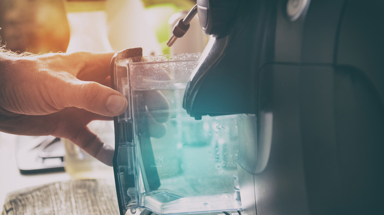 Hand removes the water refill container from espresso machine