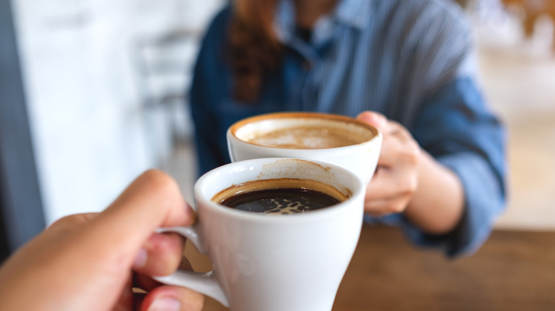 Closeup image of a woman and a man clinking coffee cups together in cafe
