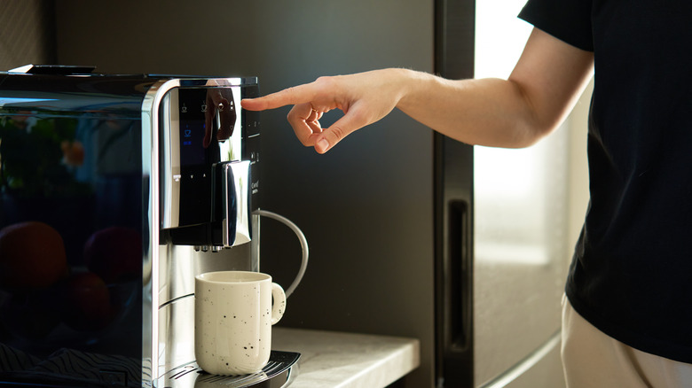 Woman preparing fresh cup of coffee with modern espresso machine.