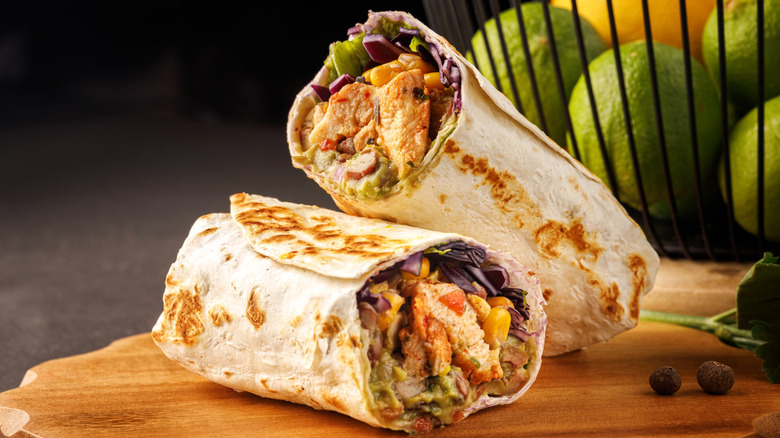 A stuffed and grilled chicken burrito on a wood board with citrus in the background.