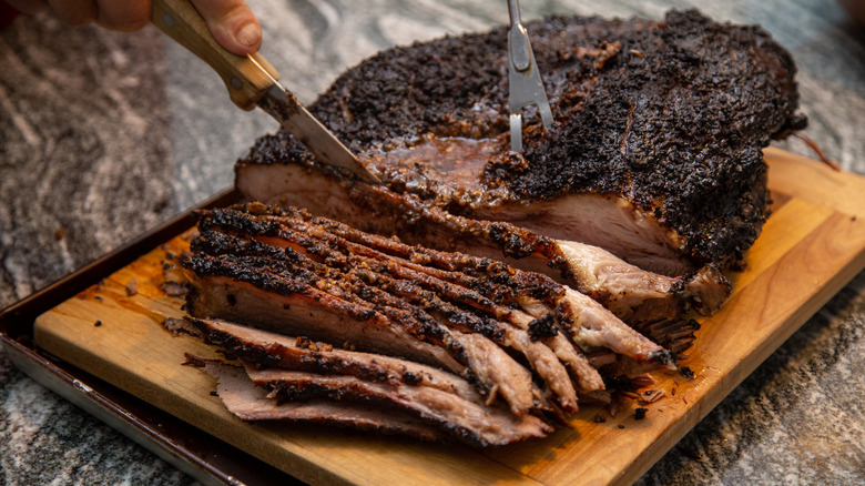 Hands slicing a beef brisket on a cutting board