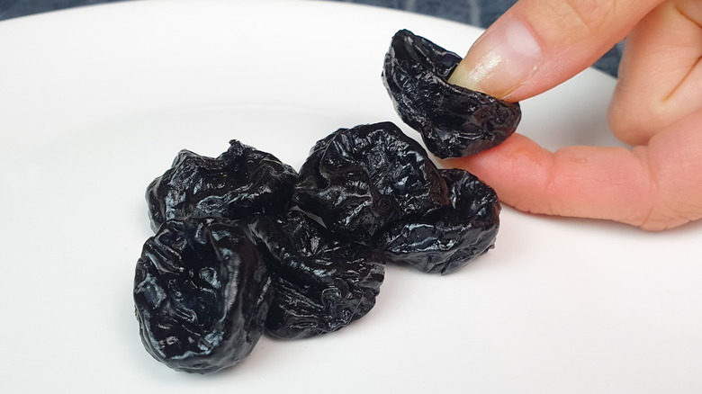 A hand picking at pile of prunes on plate