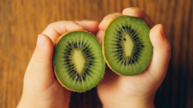 Hands holding halved kiwifruit