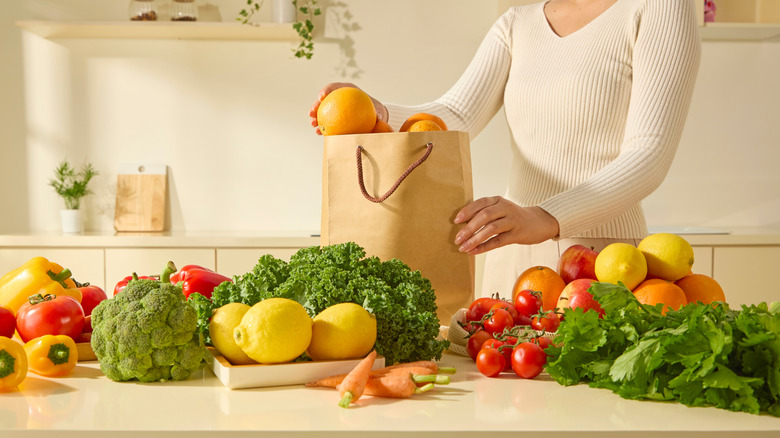 A person unloads produce onto their counter from a paper bag
