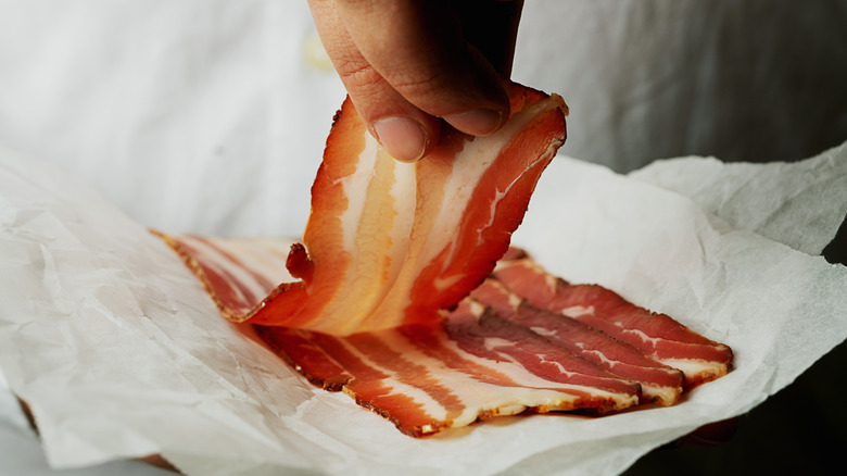 A person picking up a slice of bacon.