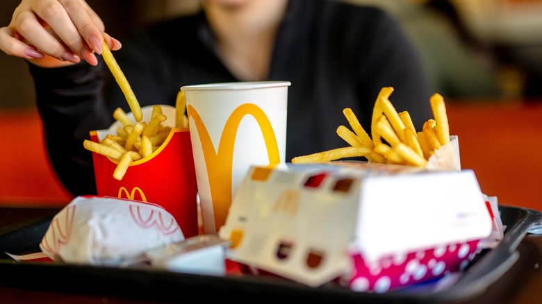 A close-up of McDonald's meals on a tray, a person taking a french fry with their body blurred in the background