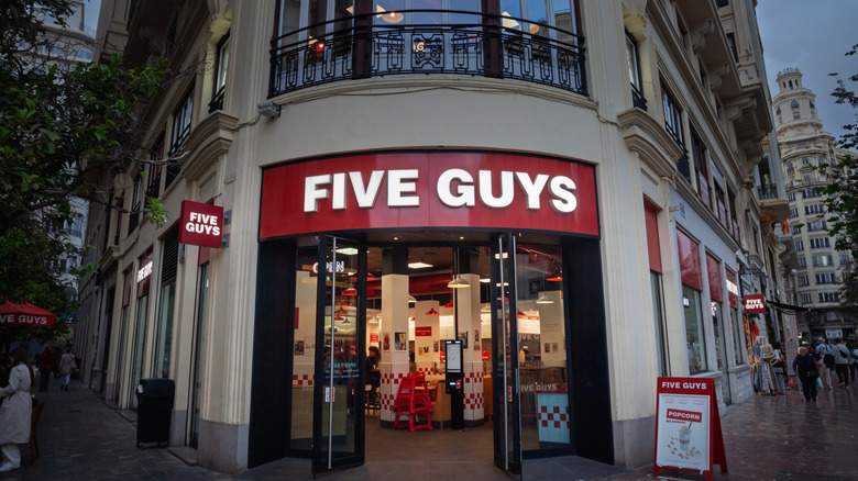 Exterior of a Five Guys burger restaurant on an urban street corner at dusk