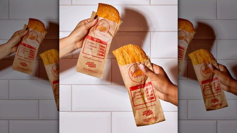 two hands holding Jamaican-style patties in Juici Patties paper wrappers