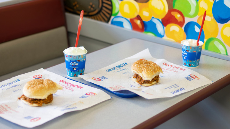 Two Dairy Queen sandwiches and two Blizzards on trays on a table.