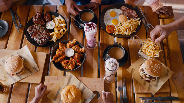 A wooden table cover with fast food items and hands around it.