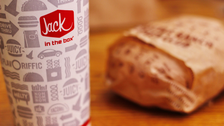 A Jack in the Box beverage cup and wrapped burger on a table.