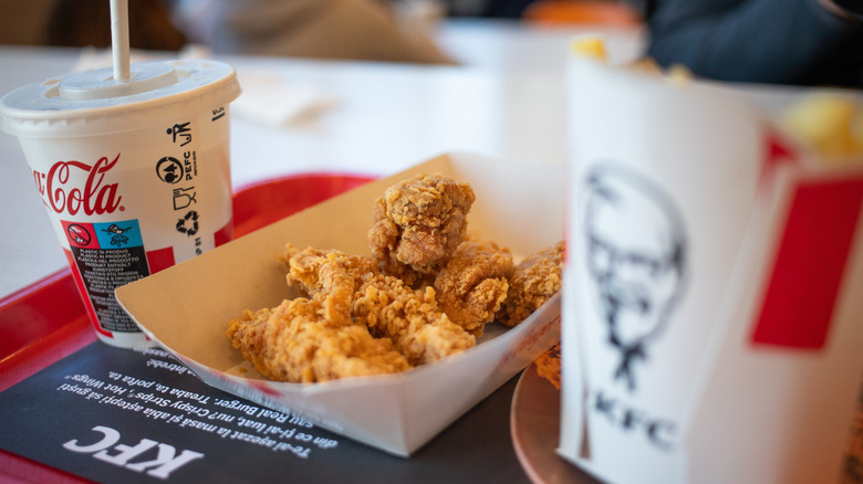 A serving of KFC chicken tenders, a Coke, and a box of fries on a tray.