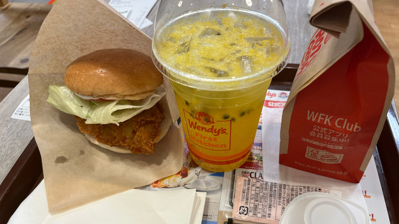 A Wendy's burger on a napkin, next to a beverage and a Wendy's bag on a tray.