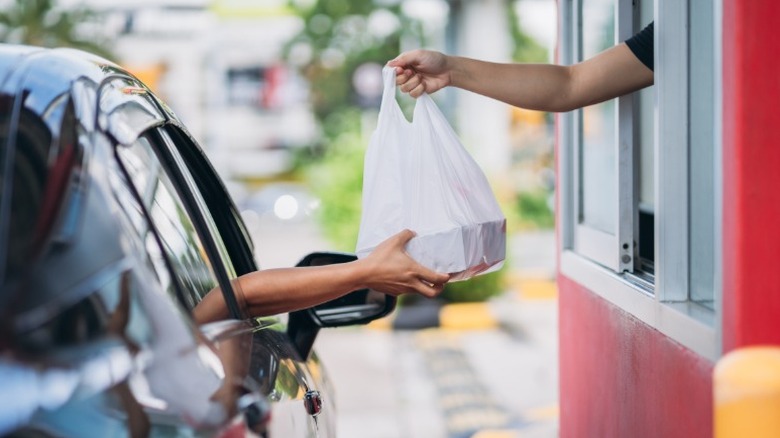 A worker hands a customer a bag at a drive thru