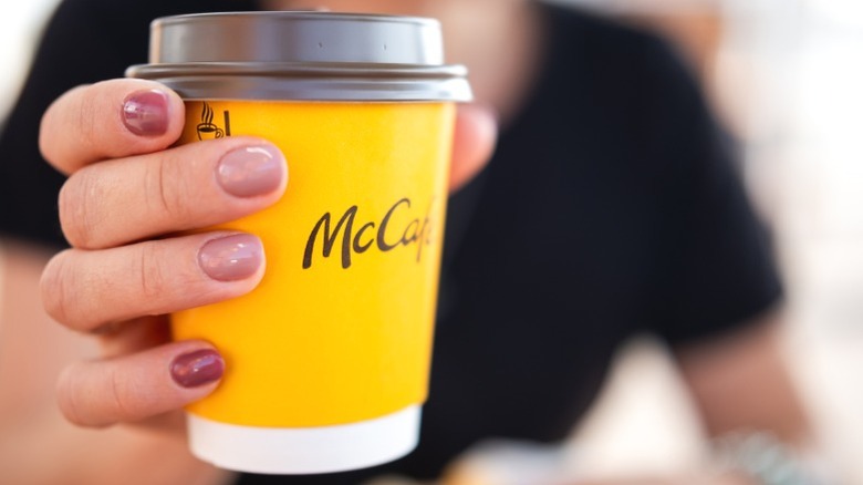 A woman holding a McCafe cup of coffee.