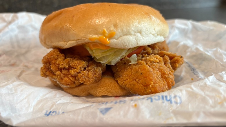 A fast food spicy chicken sandwich with lettuce on a bun in wrapper