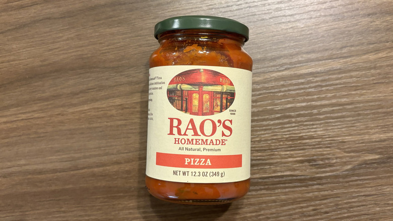 Jar of Rao's Homemade pizza sauce laying on its side on a wooden table.