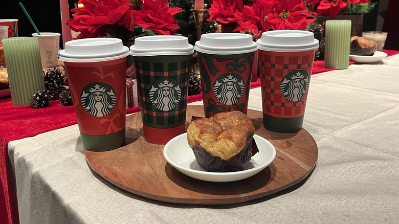 Four holiday-themed Starbucks hot cups positioned behind a cinnamon pull-apart bread