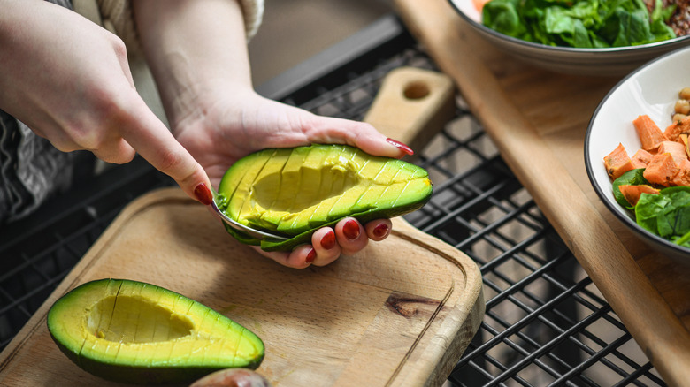 Female Using Spoon Method Removing Avocado Slices From Peel