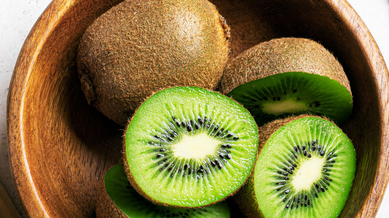 Kiwi fruits in wooden bowl. Whole fruit and half pieces of green kiwi close up.