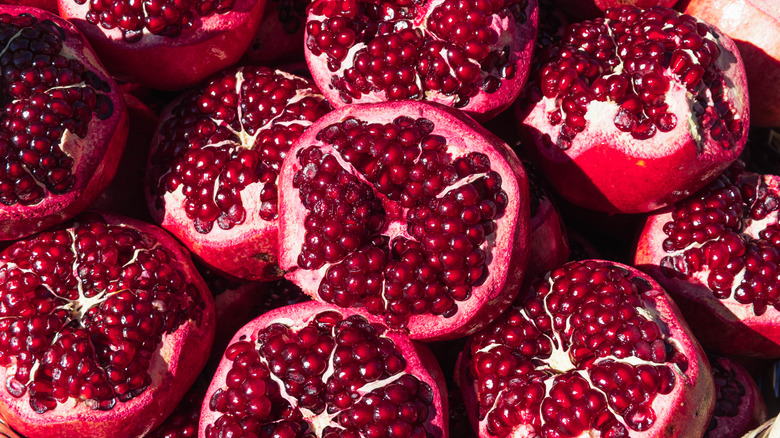 Cut fresh pomegranate and green leaves on wooden table, top view