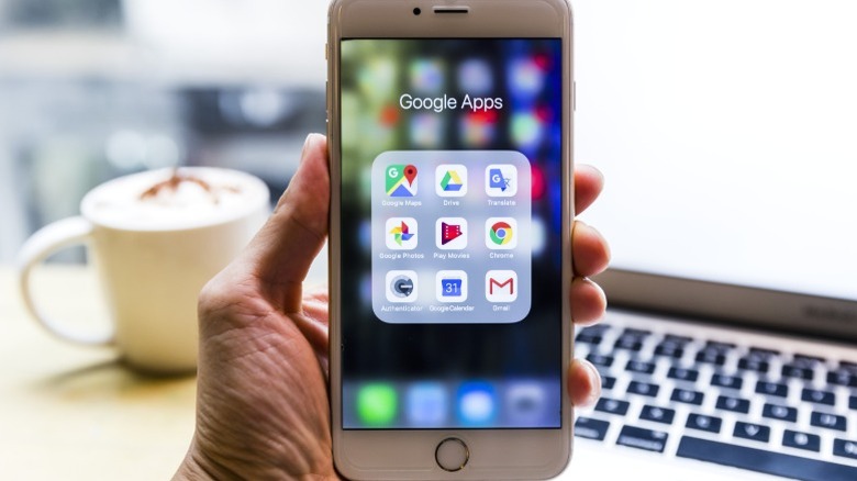A hand holding up a phone displaying Google apps.