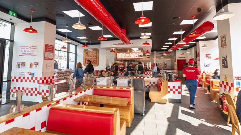 The dining room of a Five Guys with people walking around and eating.