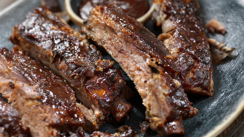 barbecued ribs on a plate with a small bowl of sauce