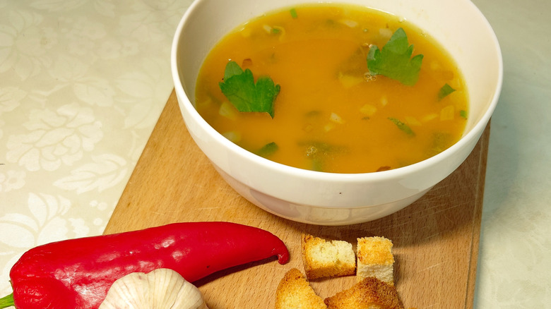 Bowl of soup on a wooden board next to pepper and breadcrumbs
