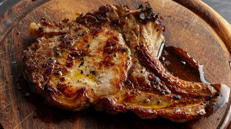 A close up of a pork chop on a wooden cutting board.