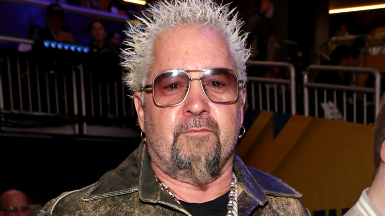 Guy Fieri wearing sunglasses and a worn leather jacket at an indoor event