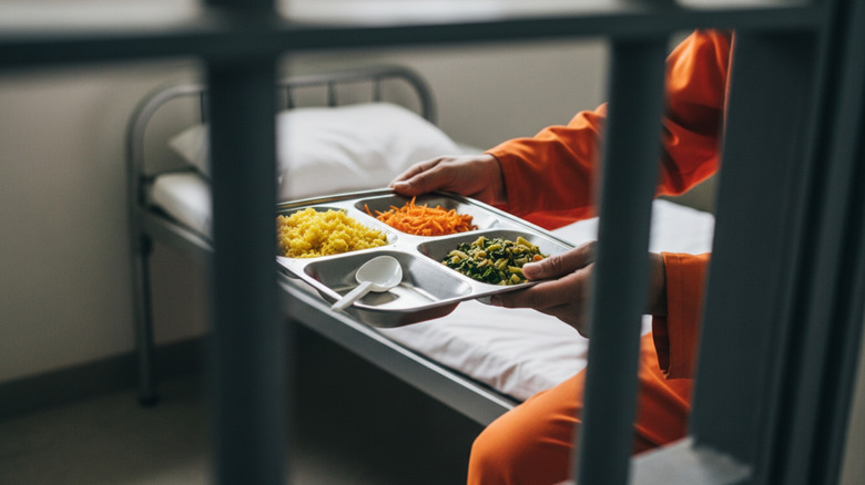 An inmate holding a tray of food in their jail cell