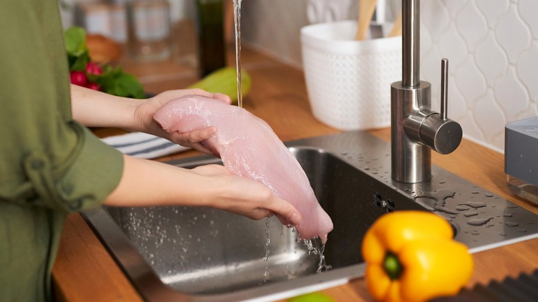 Person washing chicken under kitchen faucet