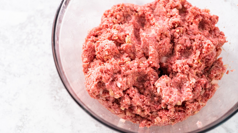 Raw ground meat in a clear bowl with diced onions