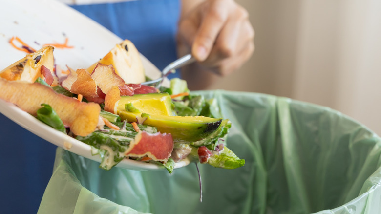 Someone throwing away a full plate's worth of food into a trash can