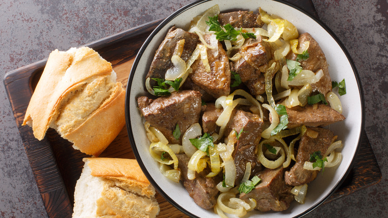 Liver and onions in a bowl next to piece of French bread