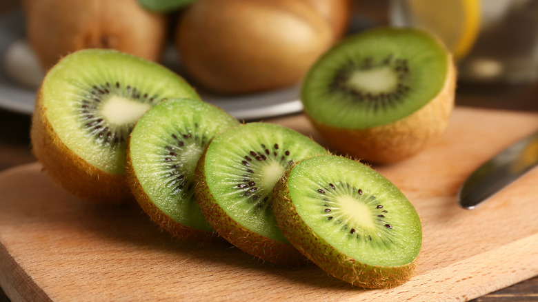 4 slices kiwi with skin on. Half a kiwi in background with whole kiwis behind
