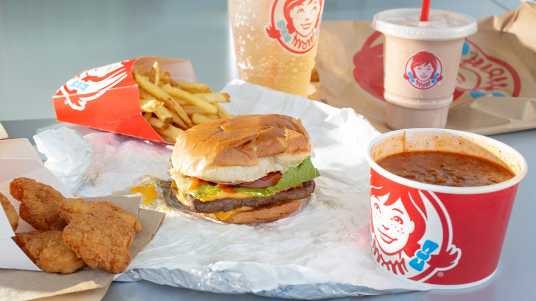 Wendy's foods including burger, fries, nuggets, chili, and frosty on a foil wrapper