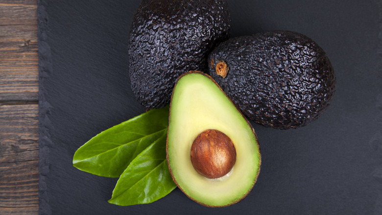 Avocados with one cut in half on cutting board