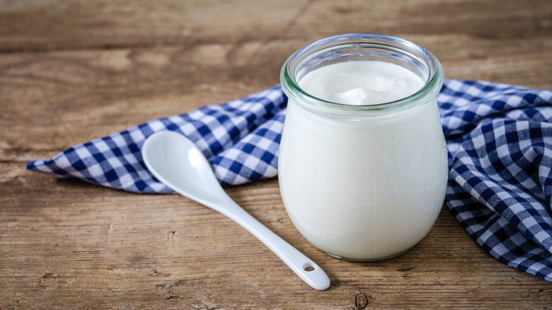 Glass of white yogurt with a ceramic spoon on wooden table