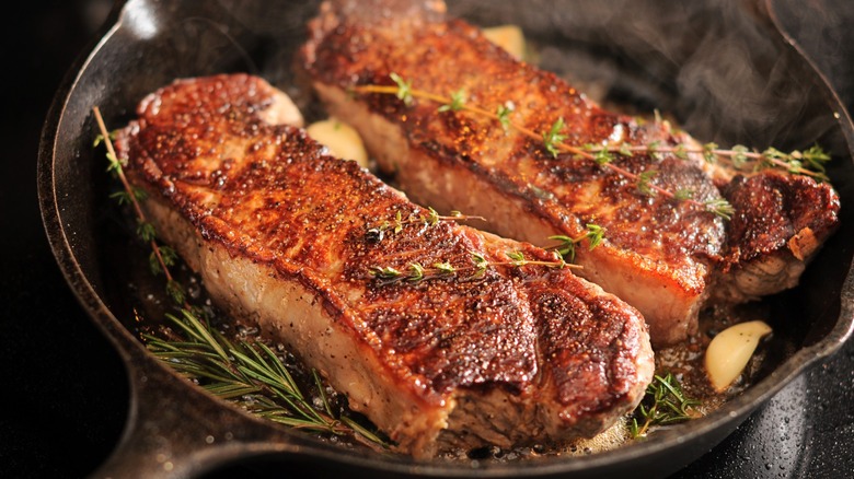 Two strip loins cook in a cast iron pan with rosemary and garlic
