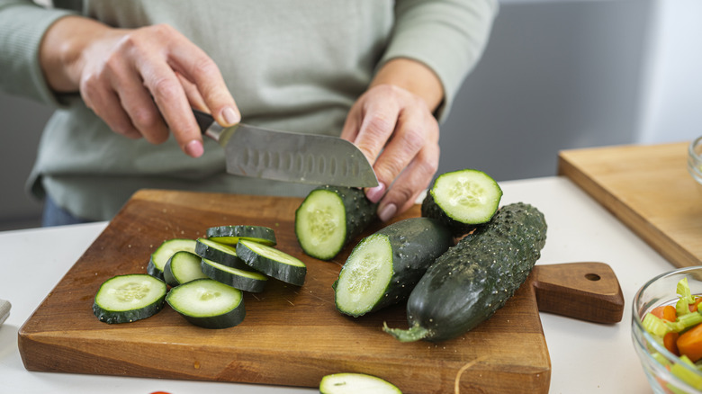 Close-up of woman's hands slicing fresh organic cucumber.
