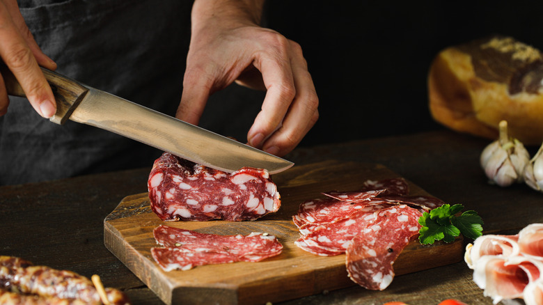 Someone slicing through cured meat with a knife.