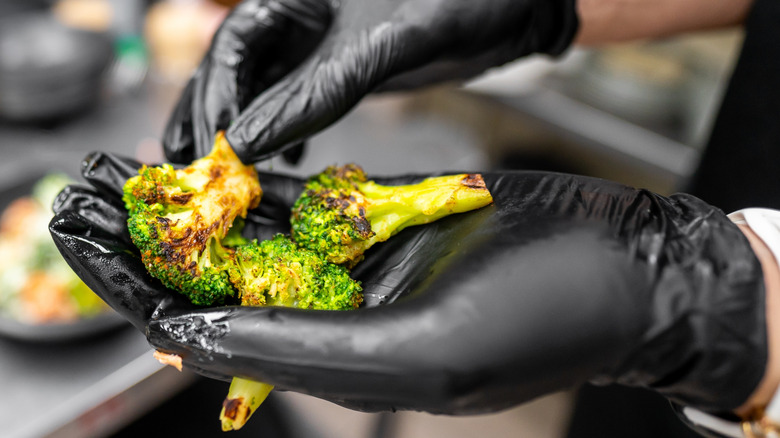 Gloved hands holding caramelized broccoli