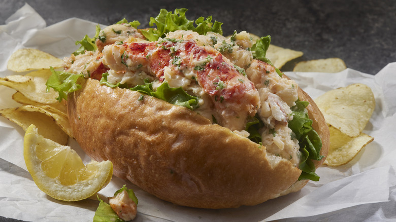 Lobster roll on white paper with scattered potato chips and a lemon wedge
